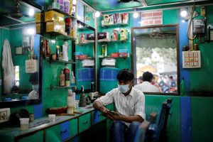 A barber wearing a protective face mask looks at his mobile phone as he waits for customers, amidst the spread of COVID-19 in the old quarters of Delhi, August 24, 2020. Photo: Reuters/Adnan Abidi